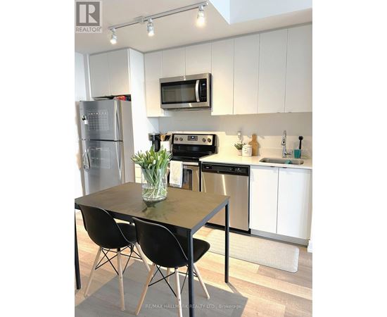 A kitchen with a table and chairs in the foreground and a refrigerator, microwave, oven, and sink in the background.