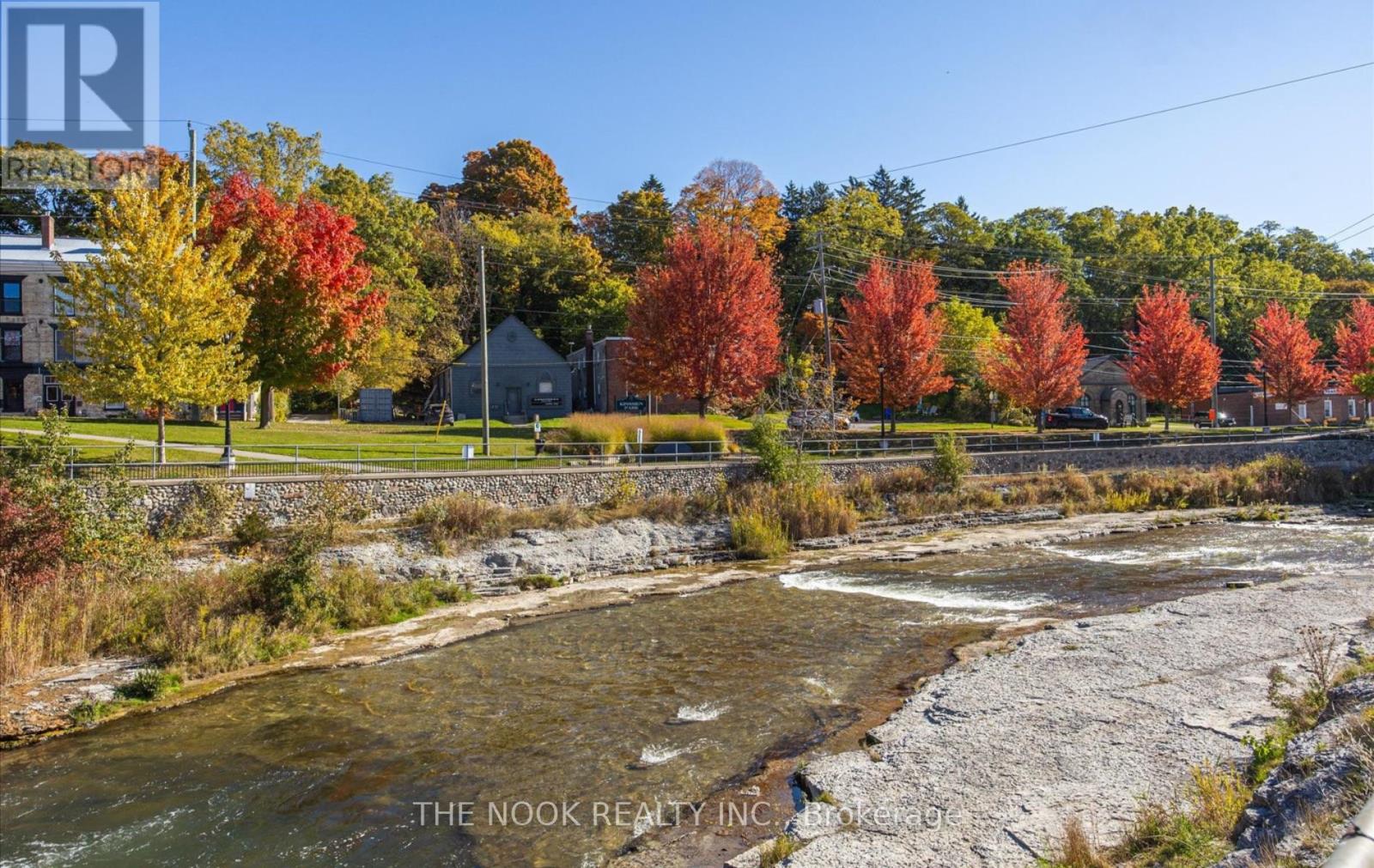 A river flows through a rocky bed with autumn trees in the background.
