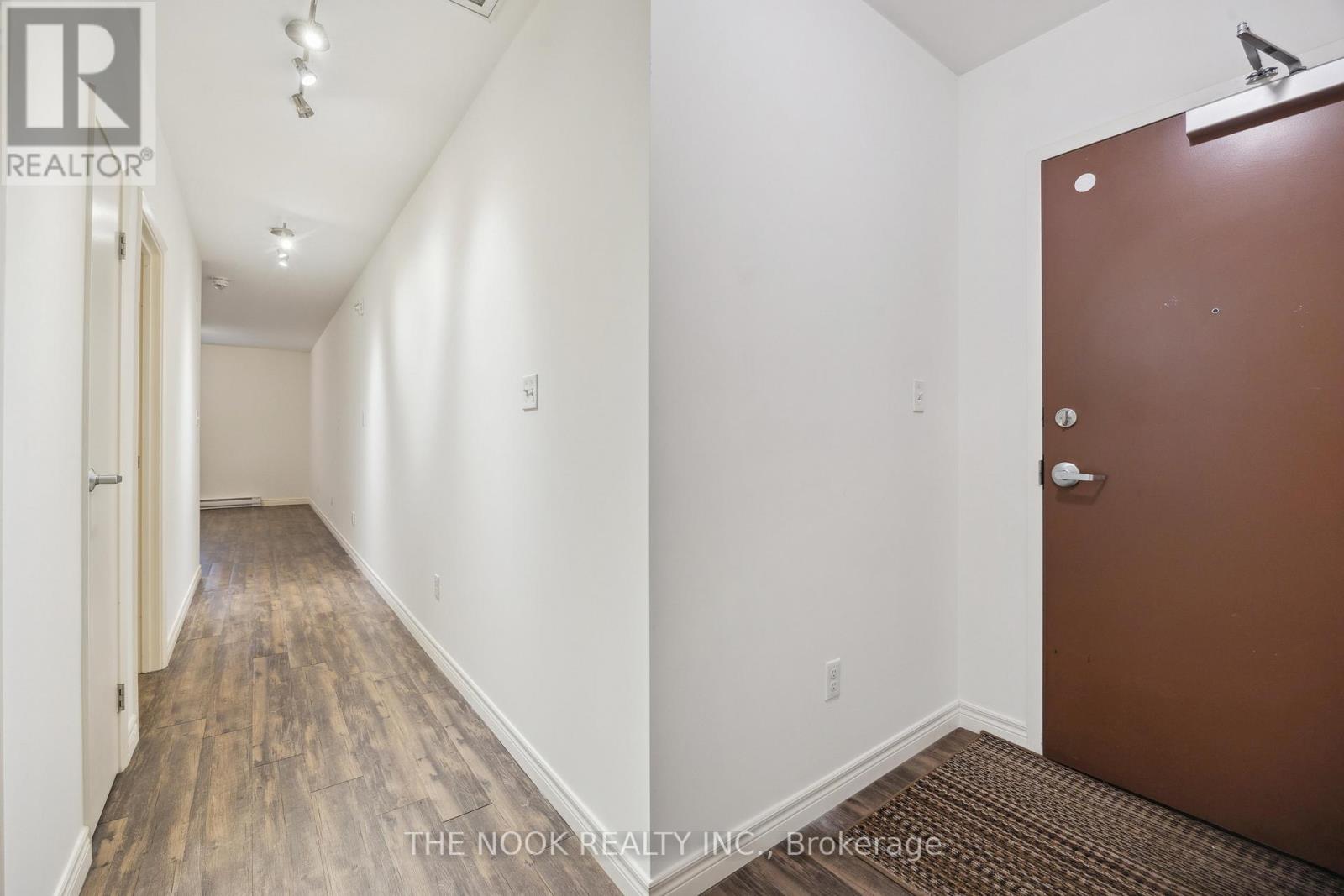 A hallway with a brown door and white walls.