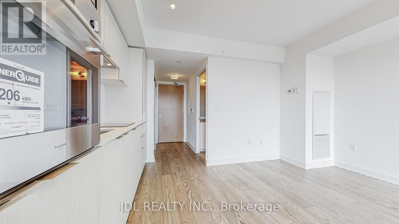 A spacious room with wooden flooring and white walls, part of a real estate listing.