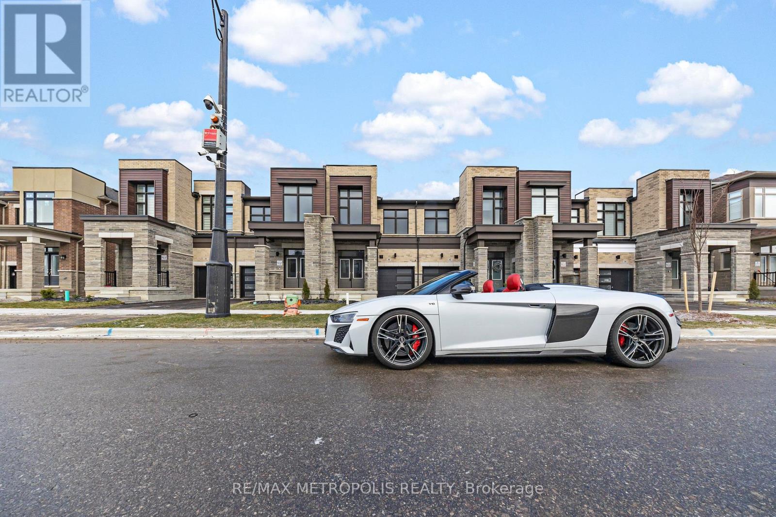 A white sports car is parked in front of a row of townhouses.