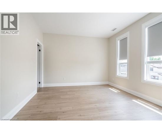 A spacious room with wooden flooring and a window on the right side.