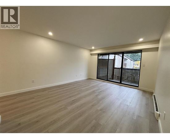 A spacious room with wooden flooring and a sliding glass door.
