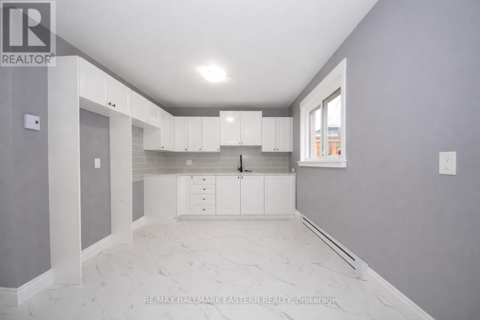 A spacious kitchen with white cabinets and marble flooring.