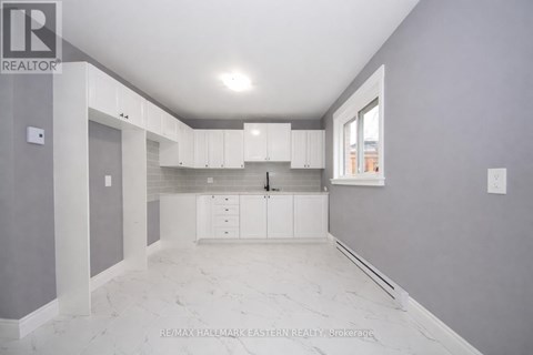 A spacious kitchen with white cabinets and marble flooring.