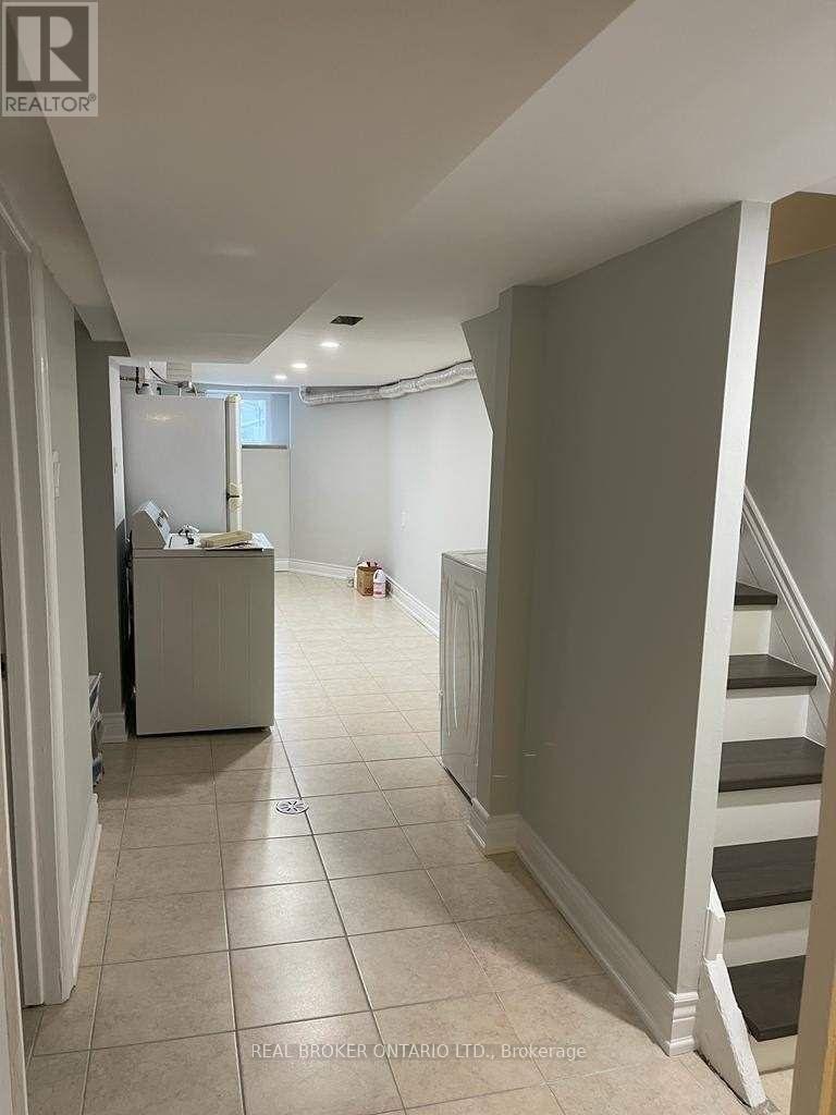 A hallway with a staircase and a refrigerator in the background.
