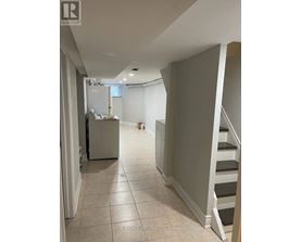 A hallway with a staircase and a refrigerator in the background.