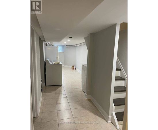A hallway with a staircase and a refrigerator in the background.