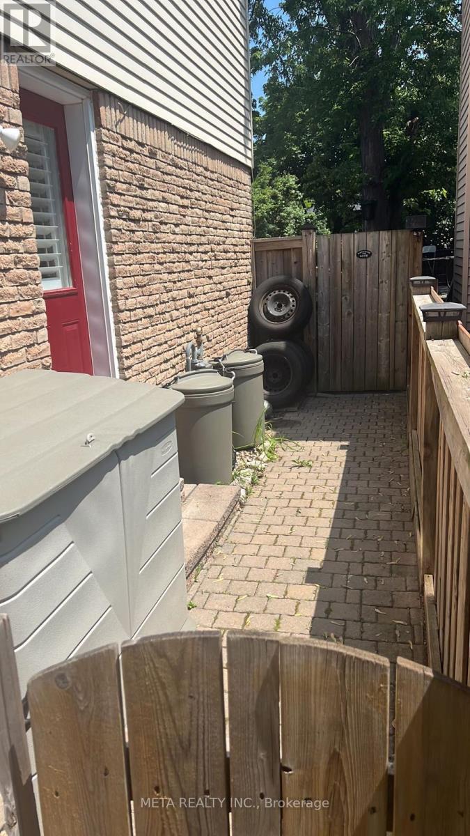 A red door is on a brick building with a trash can and a wooden fence.