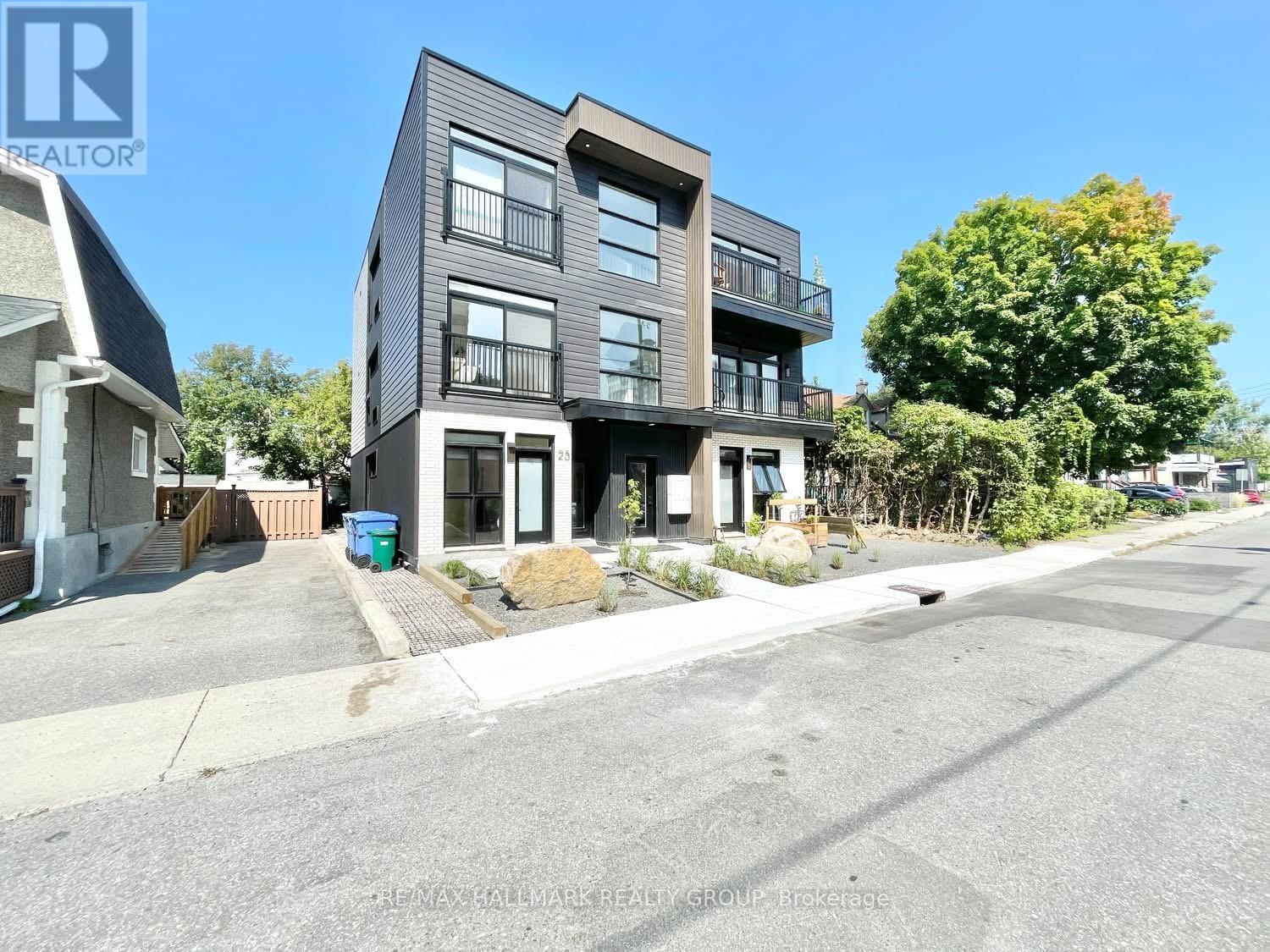 A modern two-story building with a balcony is situated on a street with a clear sky above.