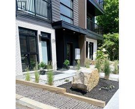 A modern house with a large rock in the front yard.
