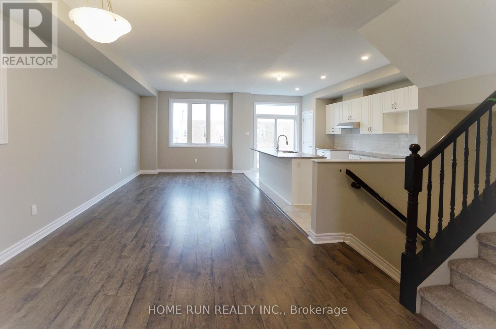 A spacious room with wooden flooring and a staircase on the right side.