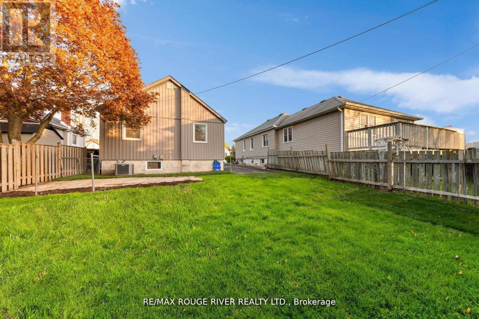 A grassy yard with two houses and a tree with orange leaves.