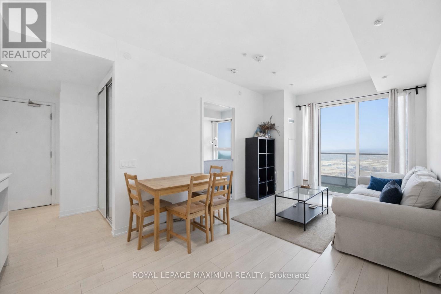 A well-lit, spacious living room with a dining table and chairs, a sofa, and a view of the ocean through the windows.