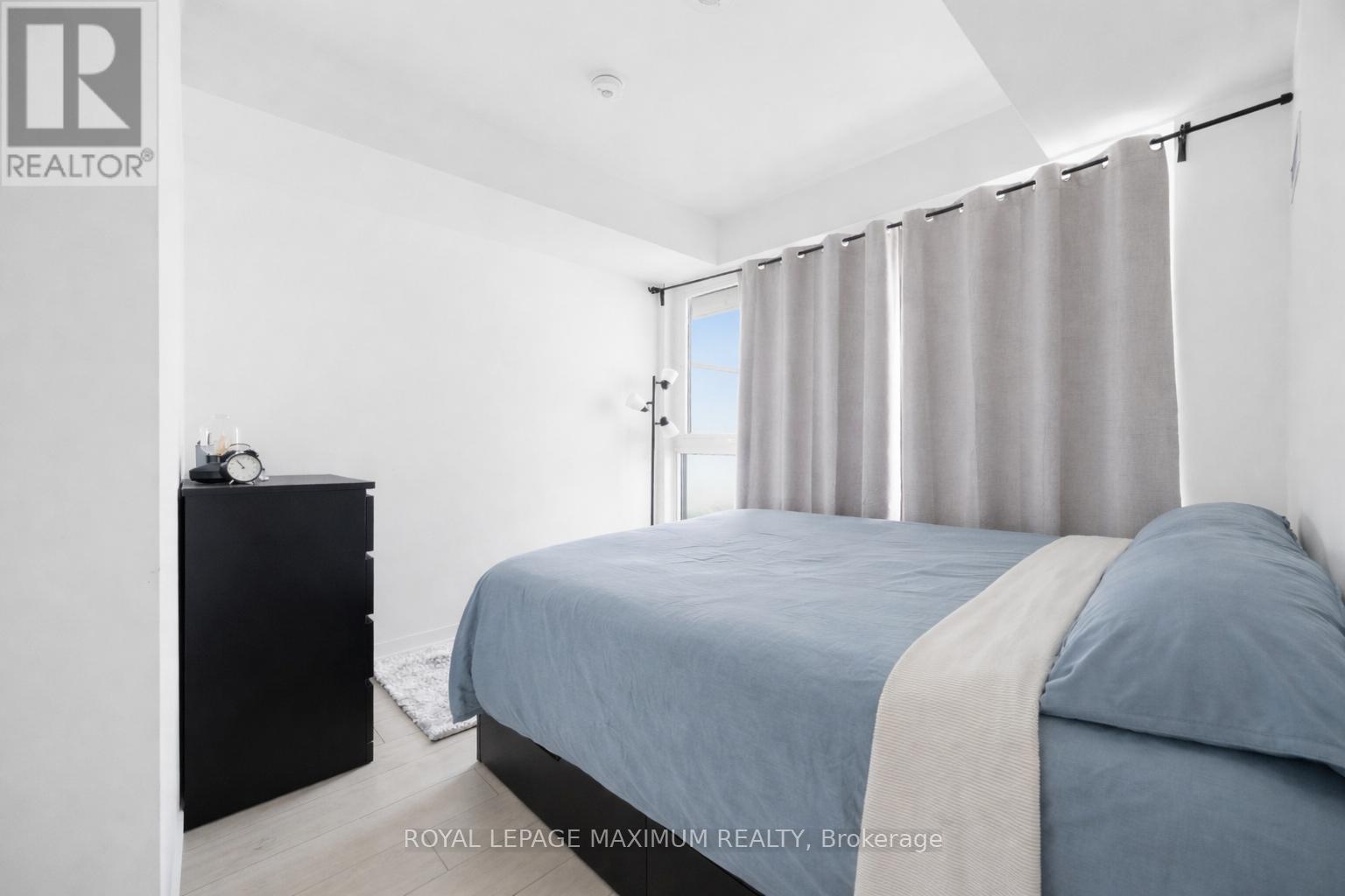 A bedroom with a bed, nightstand, and window with curtains.