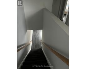 A staircase with a wooden handrail and black steps.