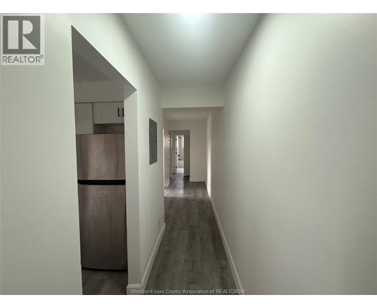 A long hallway with a refrigerator on the left and a door at the end.