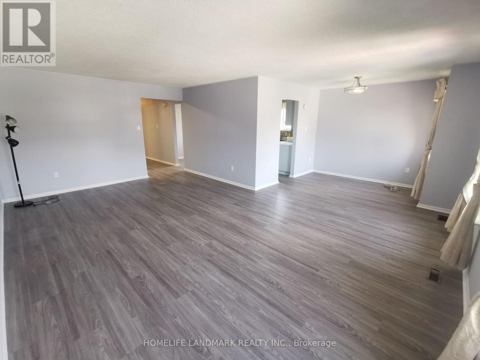 A spacious room with wooden flooring and white walls, likely for sale.