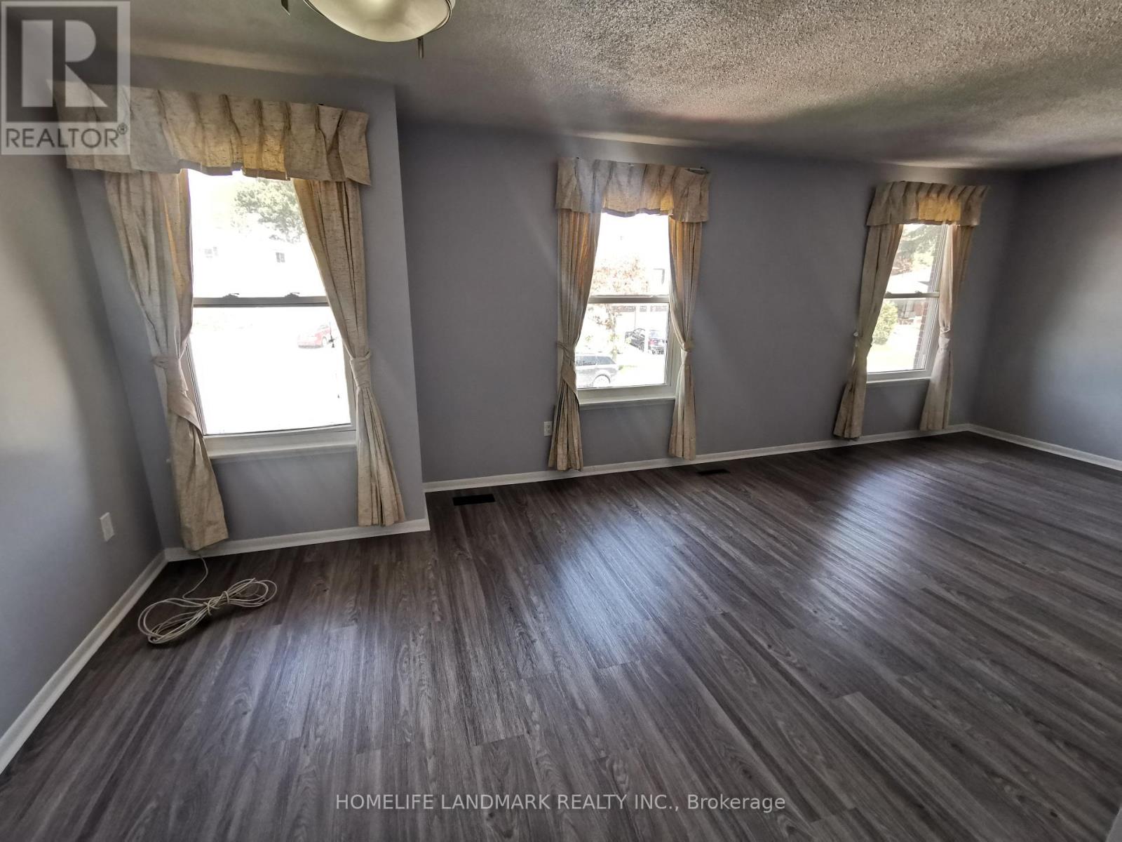A room with wooden flooring and two windows with curtains.