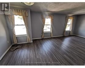 A room with wooden flooring and two windows with curtains.