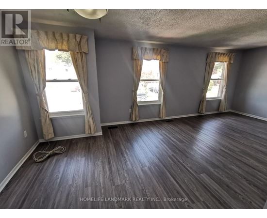 A room with wooden flooring and two windows with curtains.