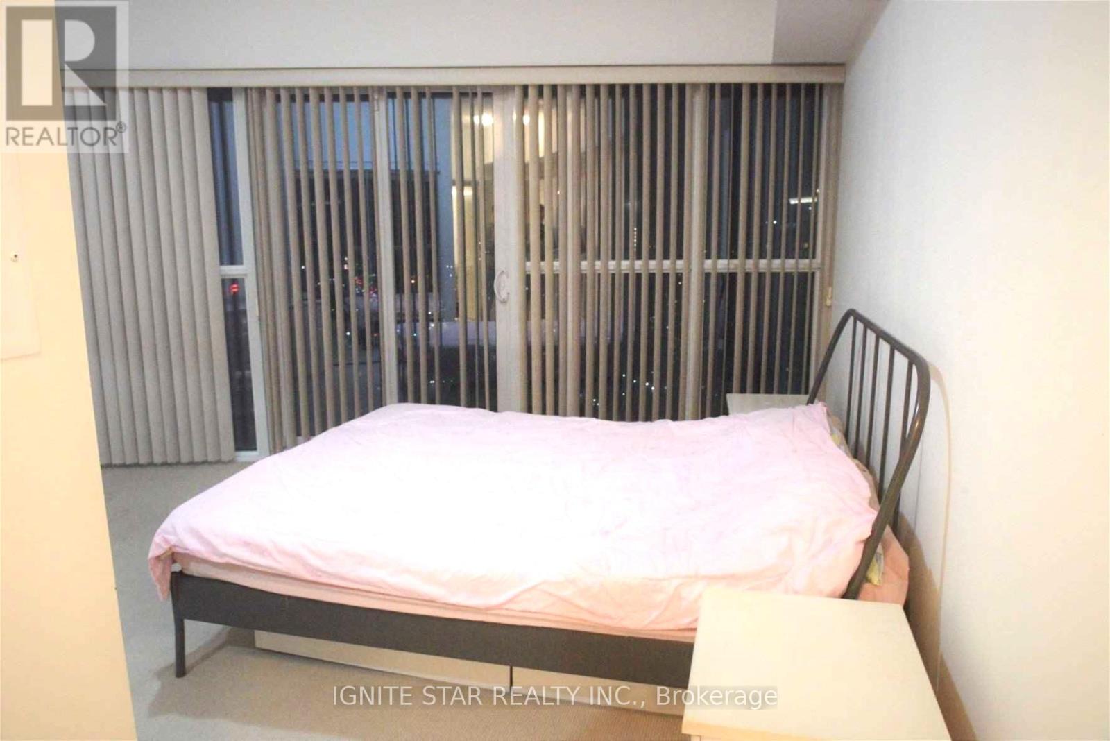 A bedroom with a metal grate window and a bed with a pink bedspread.