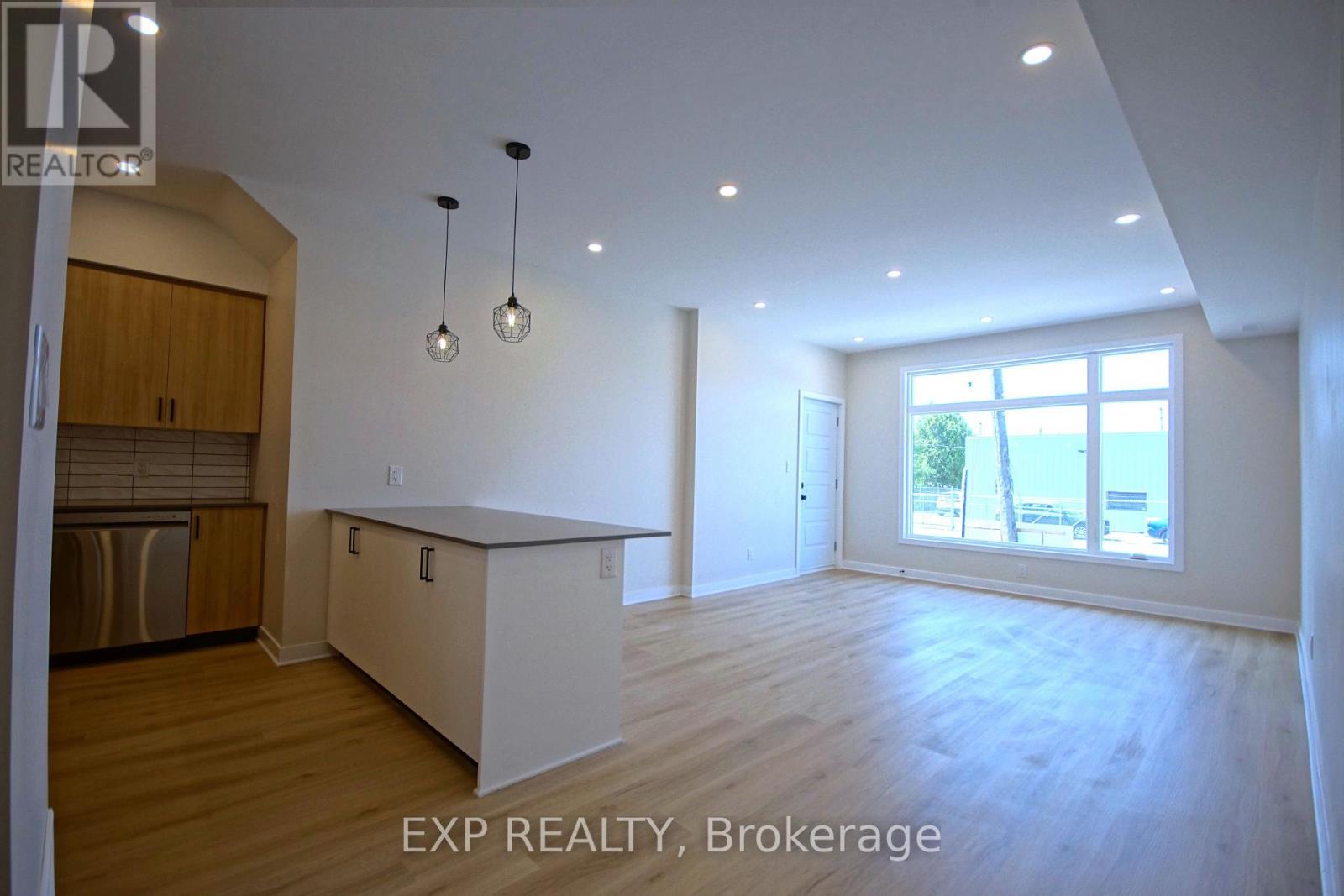 A large, empty room with wooden floors and a window overlooking a beach.