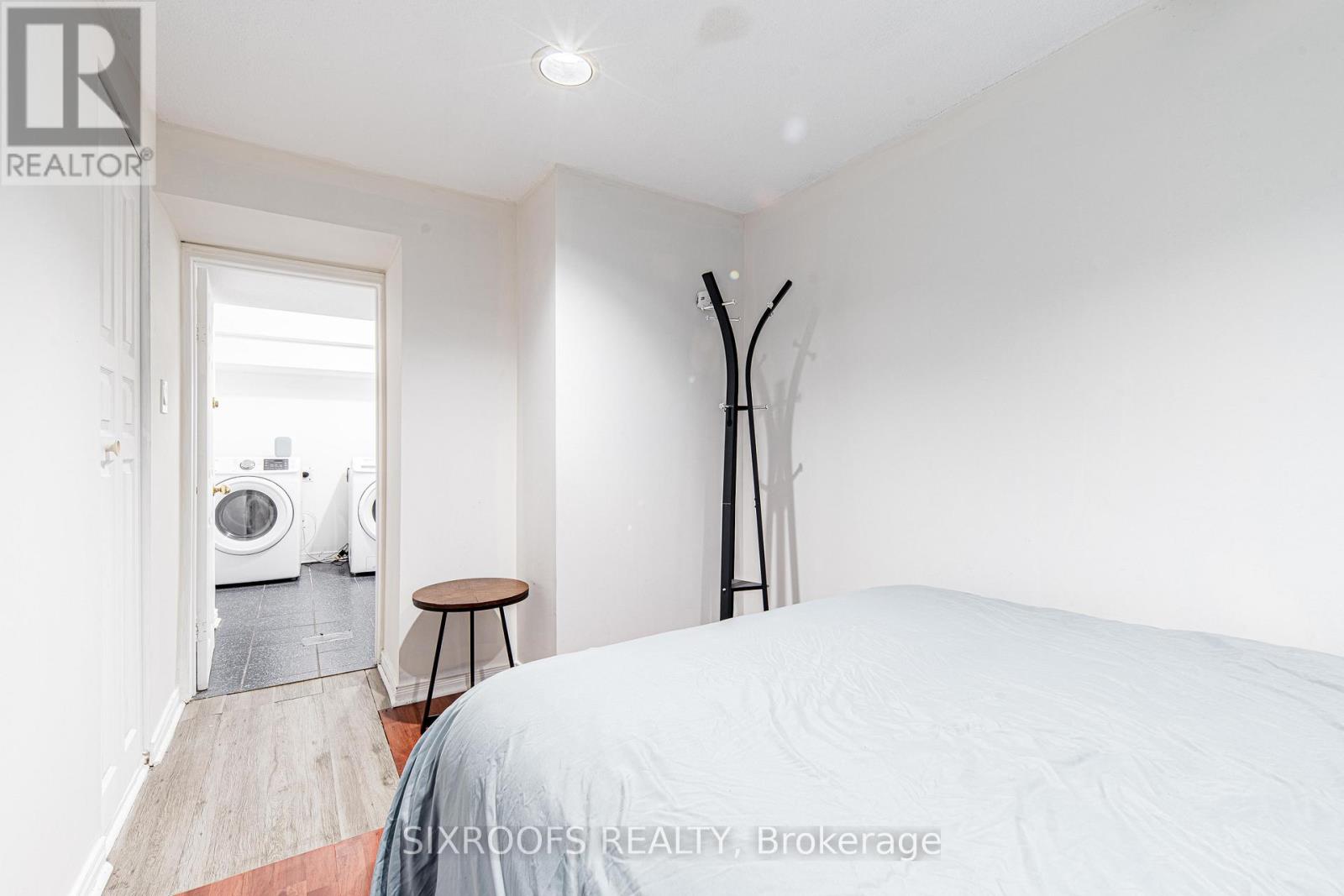 A bedroom with a large bed and a washing machine in the hallway.