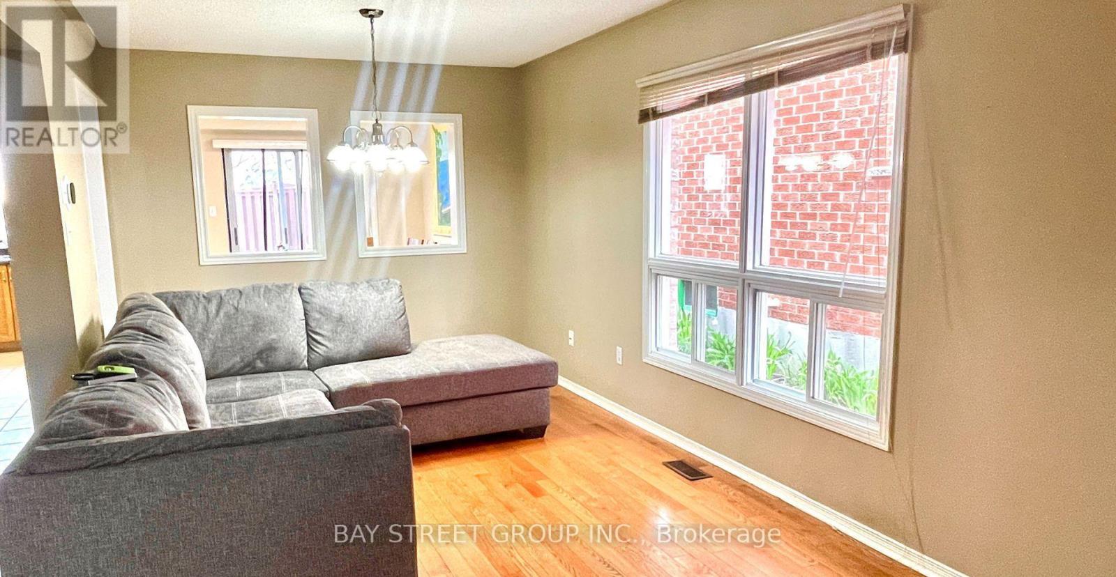 A living room with a grey couch and a window with a view of a brick building.