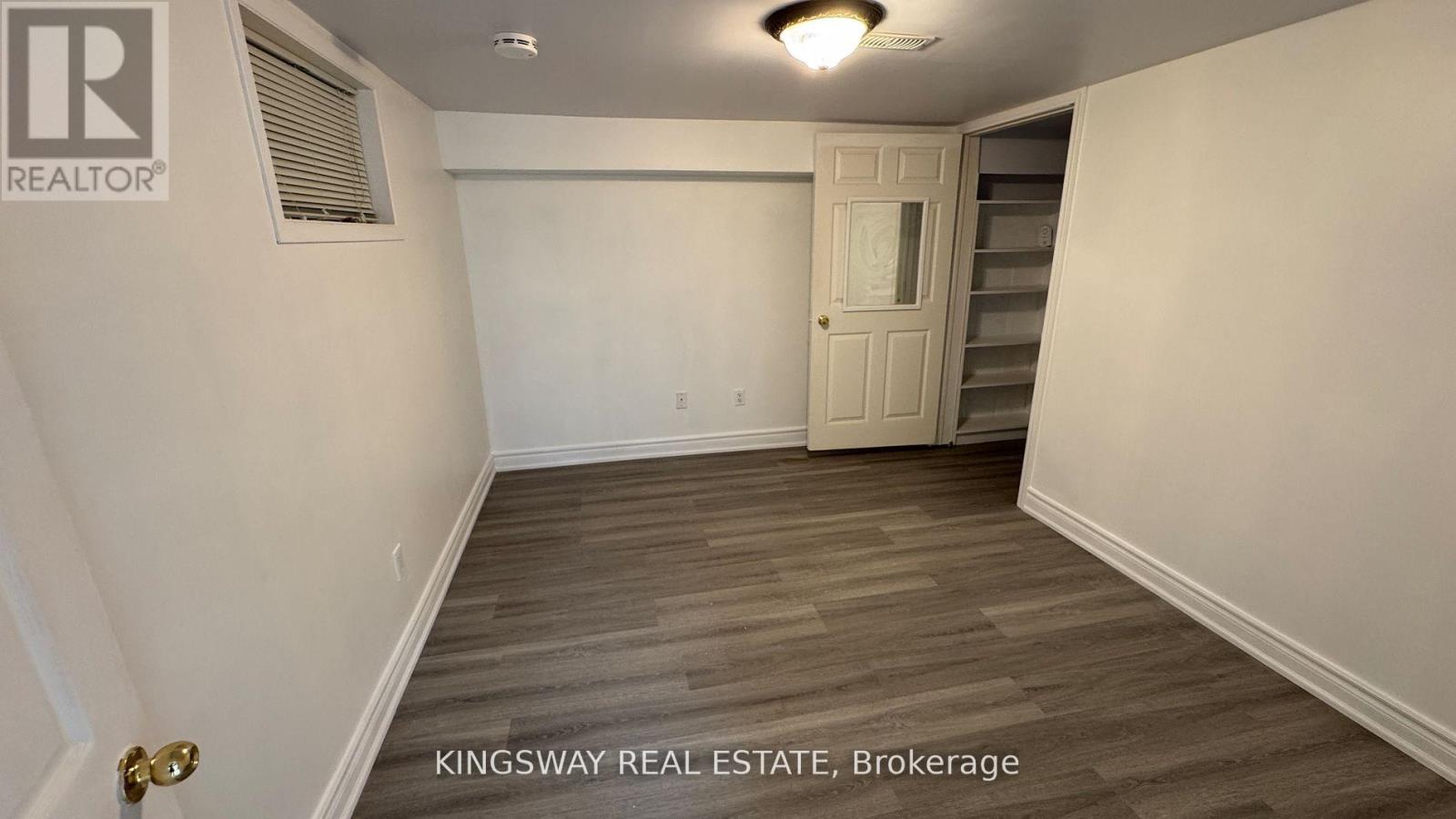 A brokerage sign is on the wall of a white room with a wooden floor and a white door.