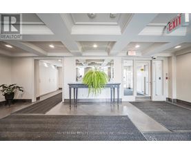 A hallway with a plant in the middle and a red exit sign above.
