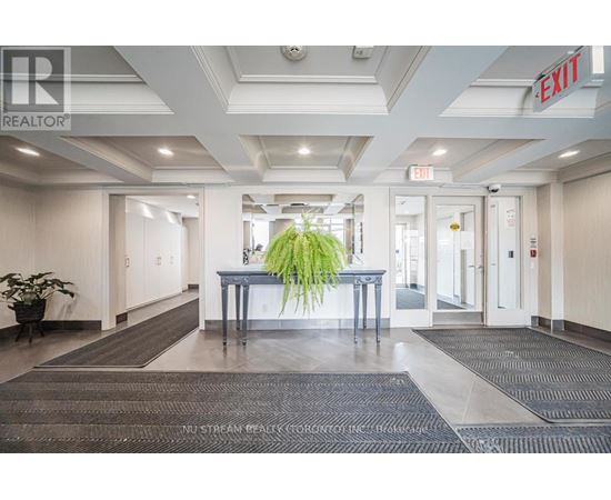 A hallway with a plant in the middle and a red exit sign above.