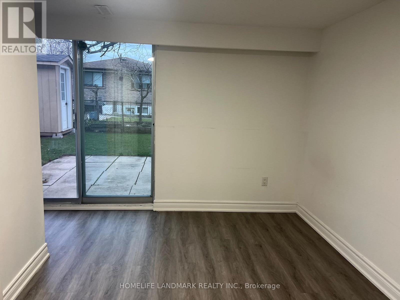A room with wooden flooring and a sliding glass door leading to a backyard.