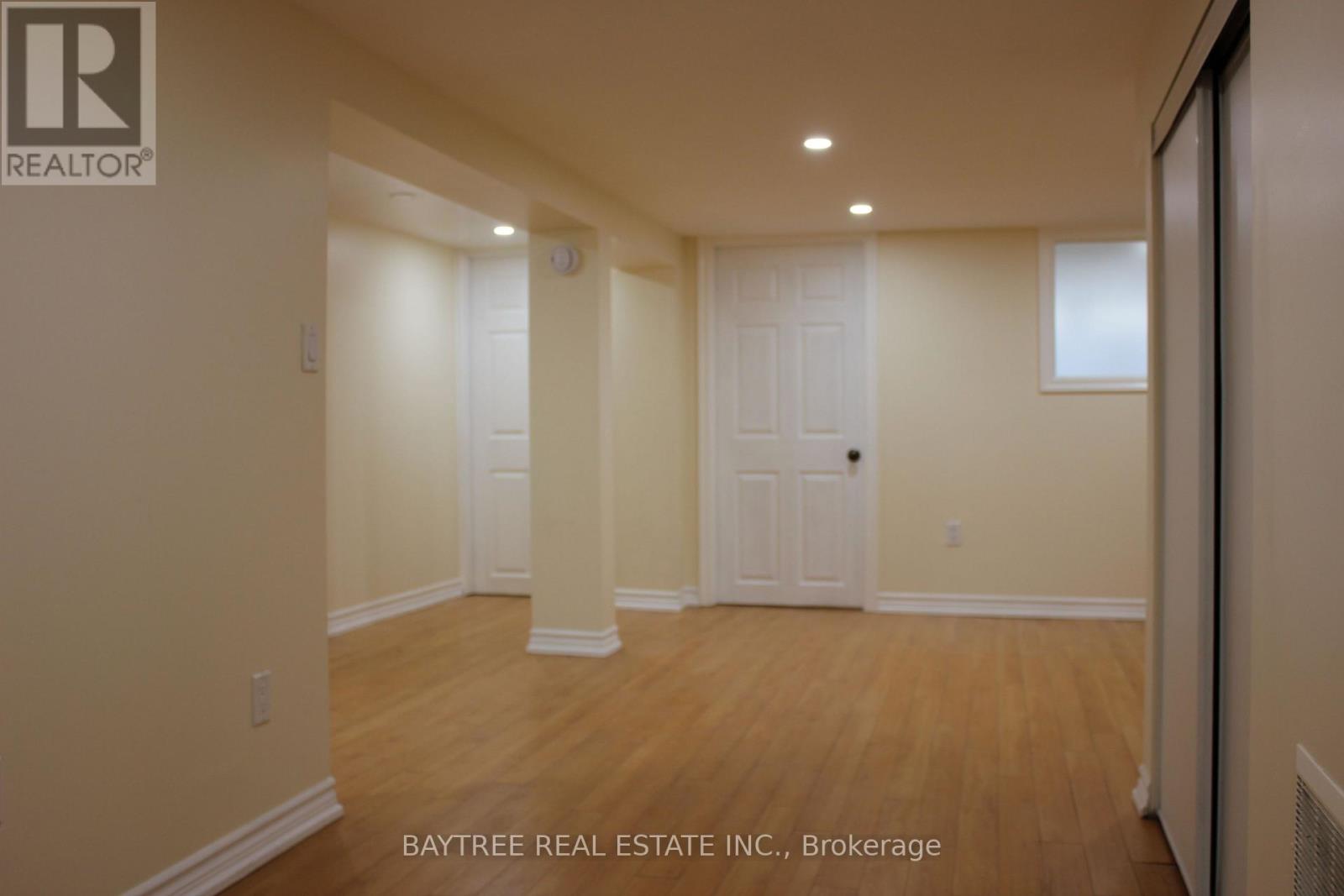 A spacious room with wooden floors and white walls, with a door on the right side.