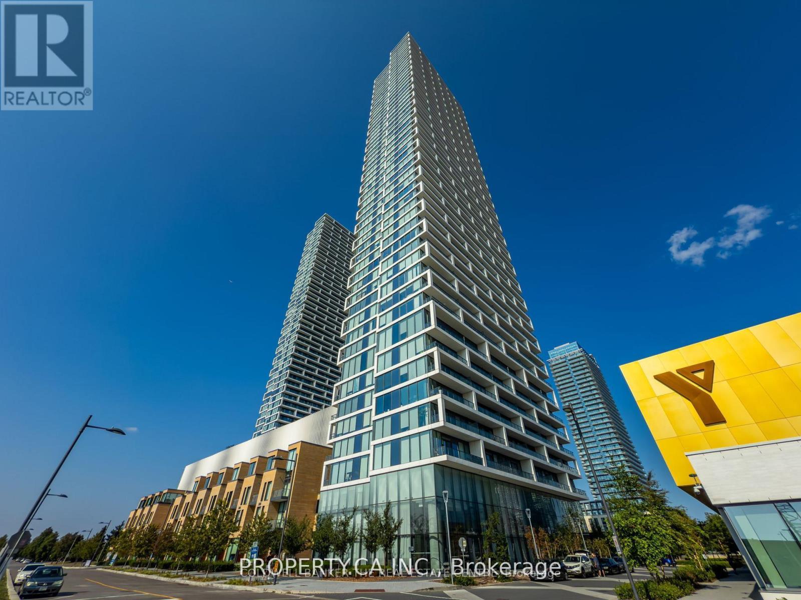 A tall building with a glass facade stands in front of a clear blue sky.