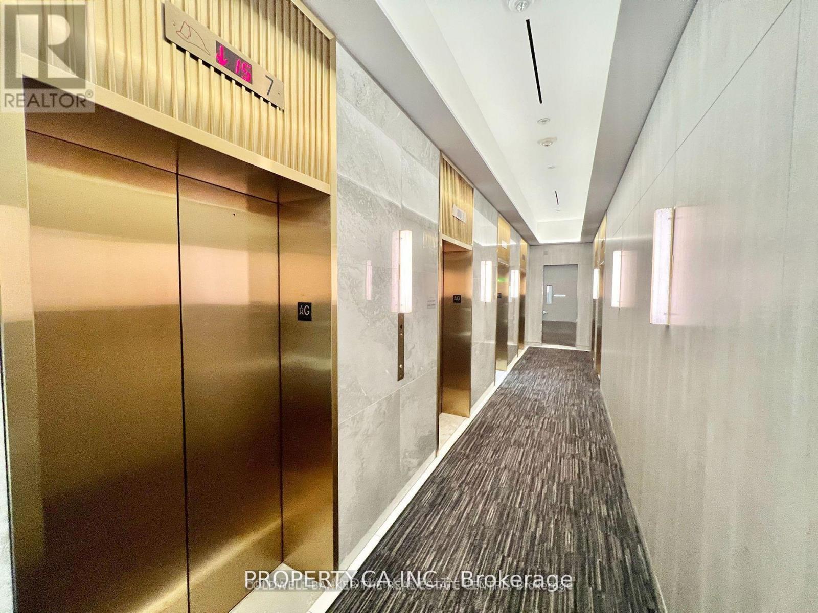 A long hallway with a carpeted floor and a row of elevators on the left side.