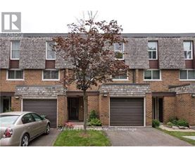 A grey car is parked in front of a brick building with a tree in front of it.