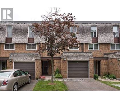A grey car is parked in front of a brick building with a tree in front of it.
