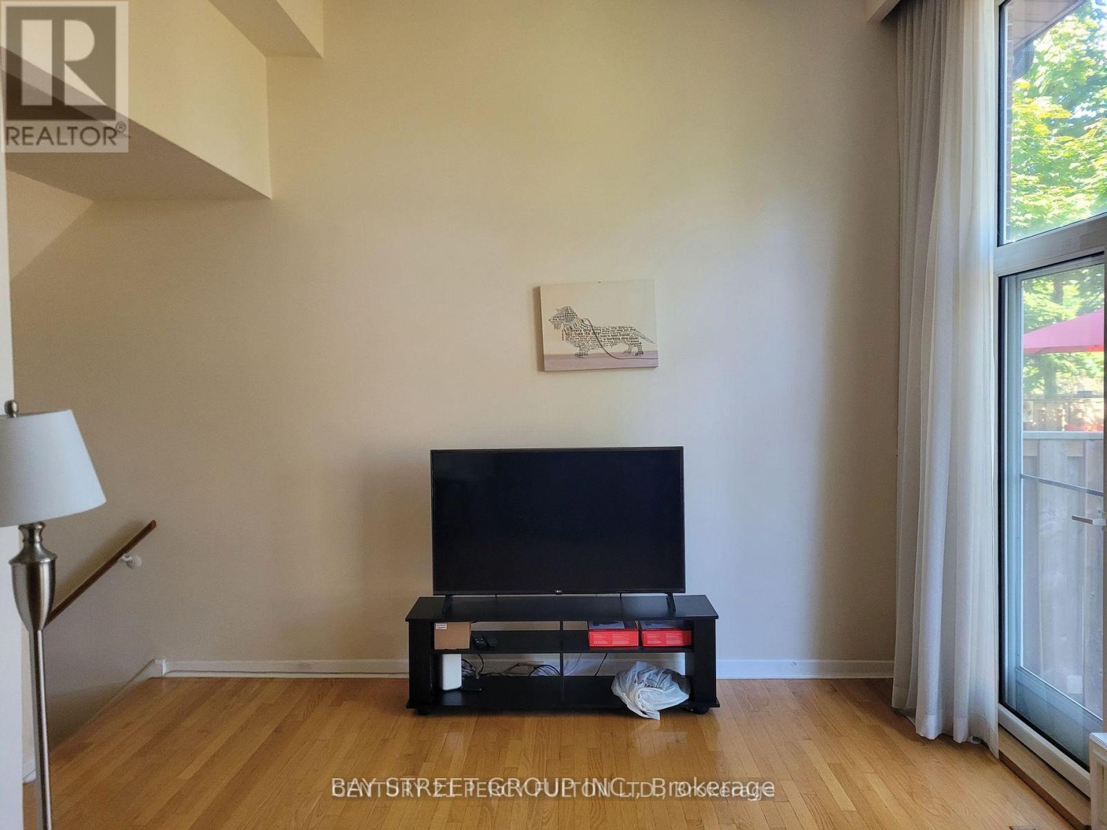 A black television sits on a wooden stand in a room with a painting on the wall.