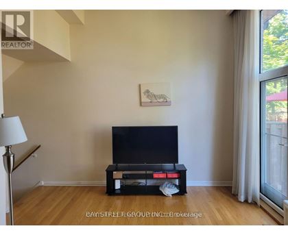 A black television sits on a wooden stand in a room with a painting on the wall.