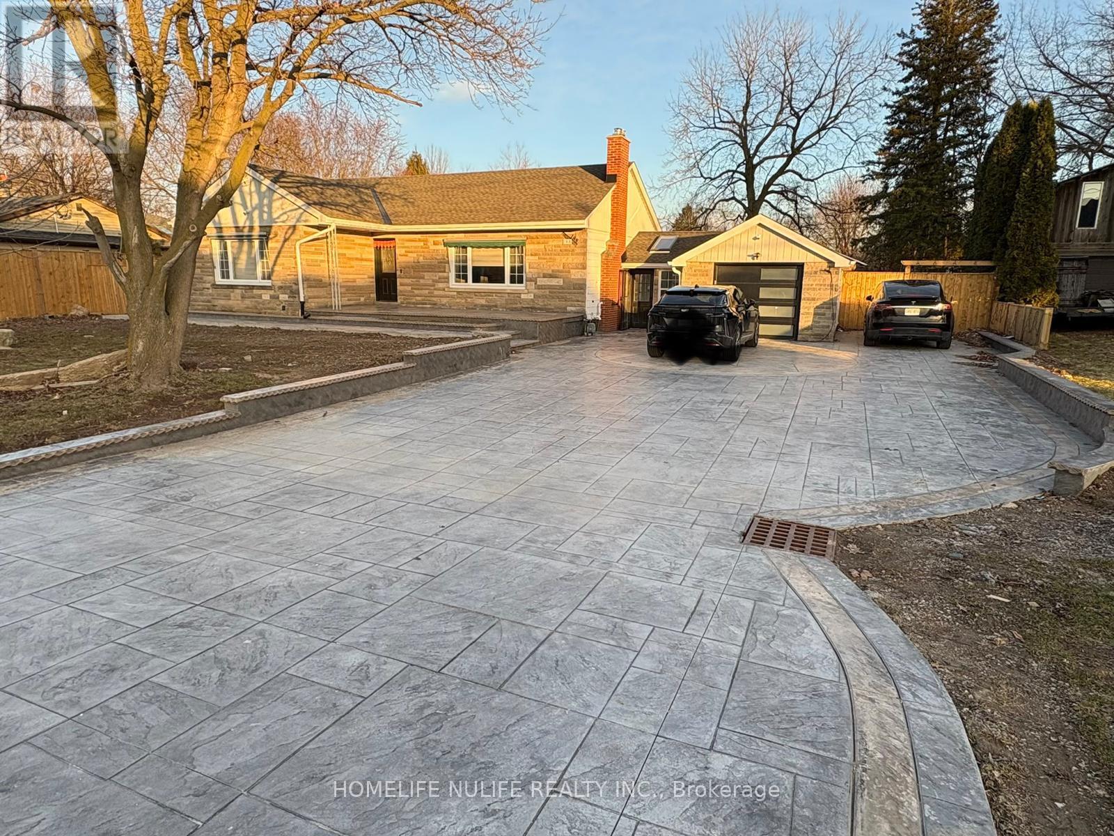 A driveway with a stone pattern leads to a house with a garage.
