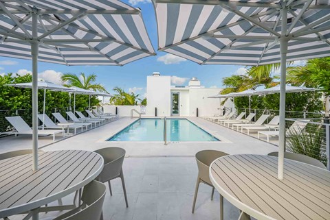 A pool area with a white umbrella and chairs.