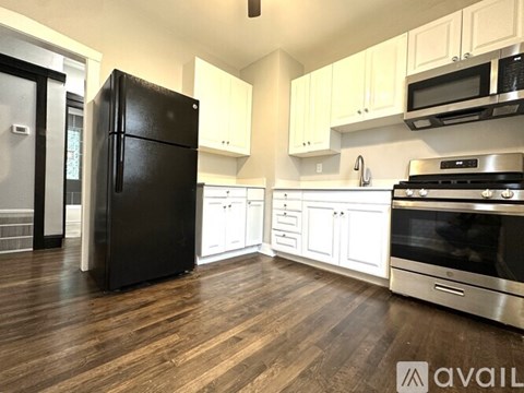 A black refrigerator stands in a kitchen with white cabinets and stainless steel appliances.