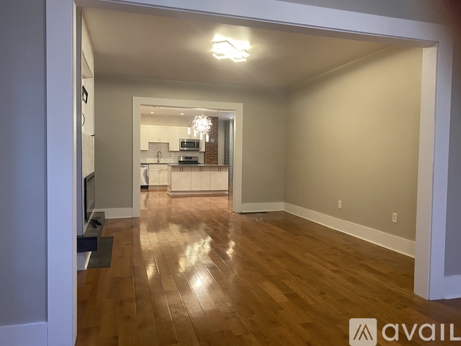 A spacious living room with hardwood floors and a kitchen in the background.