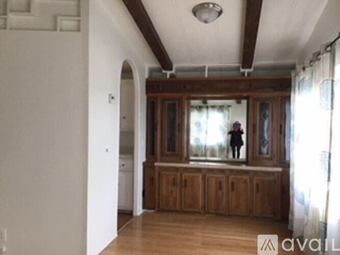 A person stands in a large room with wooden cabinets and a window.