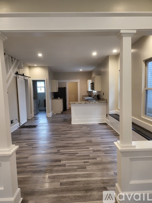 A spacious room with wooden flooring and white columns.