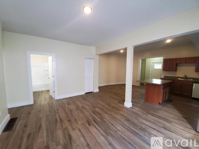 A room with wooden flooring and a kitchen area in the background.