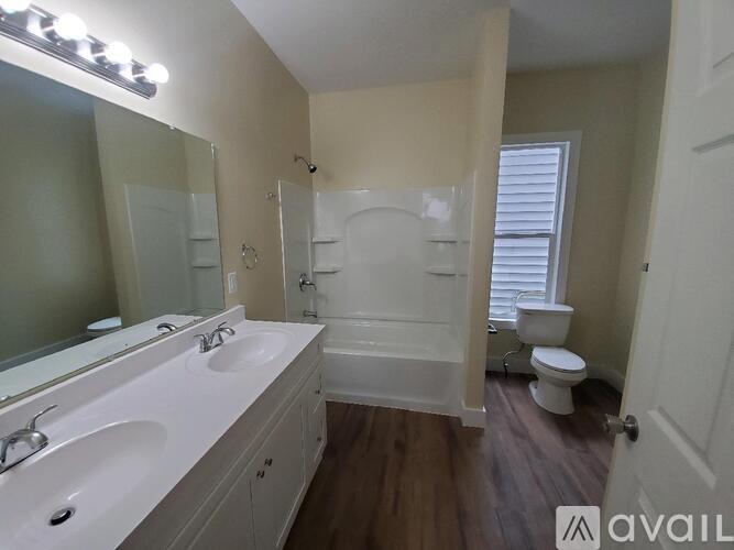 A bathroom with a white tub and sink, a toilet, and a window with blinds.