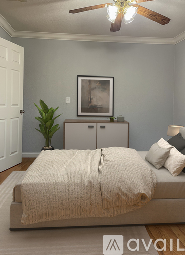 A bedroom with a bed, a plant, and a framed picture on the wall.