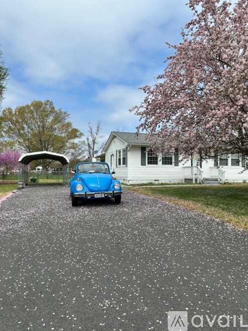 A blue car is parked on a gravel driveway in front of a white house.